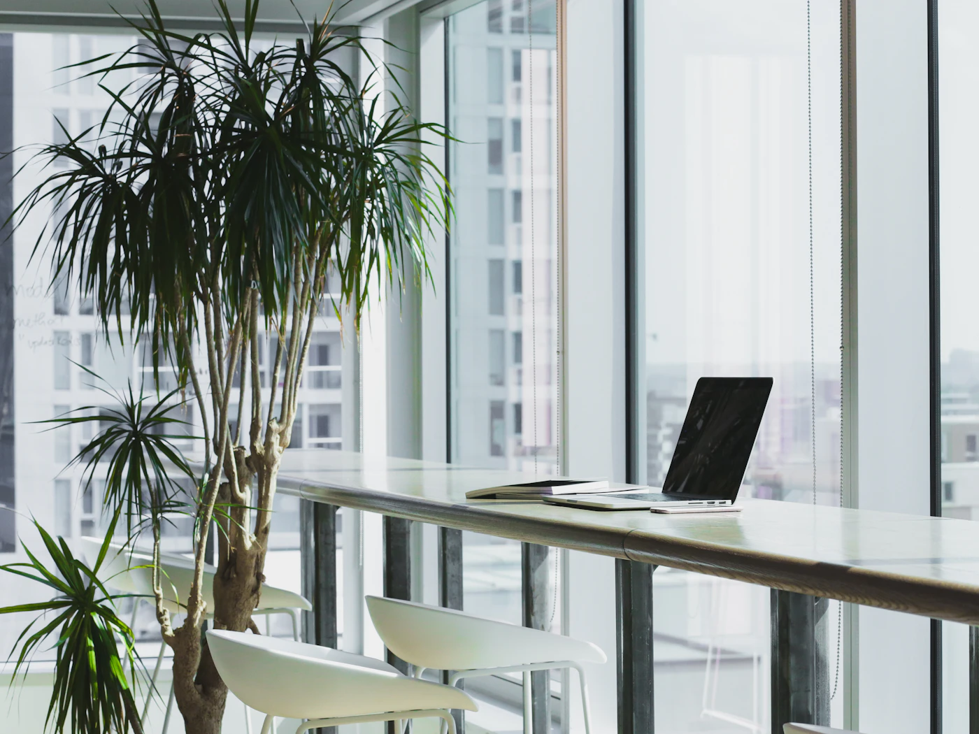 A laptop on a desk pushed up against a bright floor-to-ceiling window